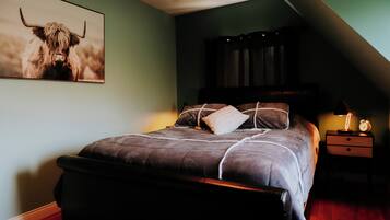A bedroom with a bed, pillows, a nightstand with a lamp, a framed picture on the wall, and a sloped ceiling.