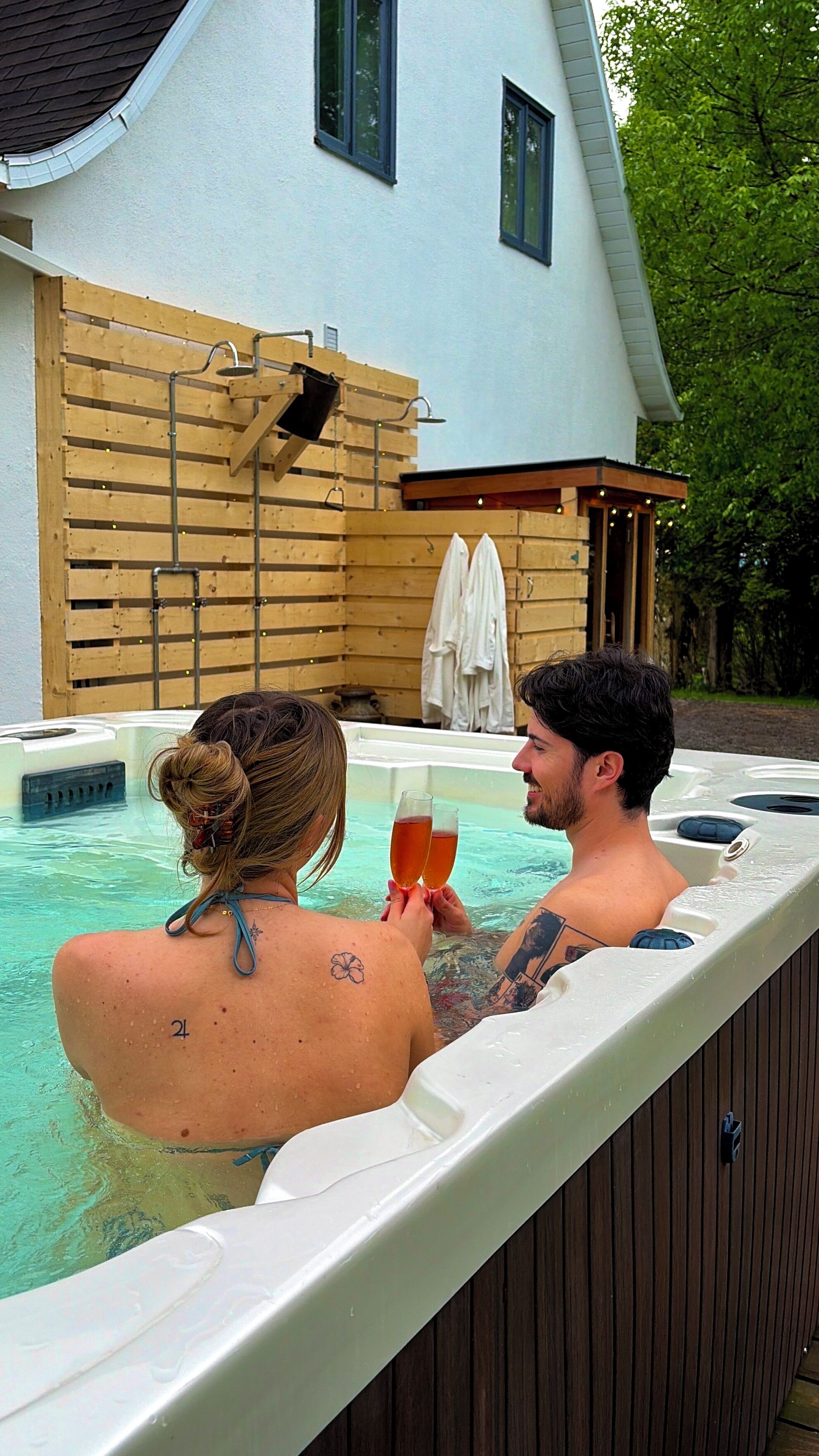 A couple in a hot tub with a wooden deck and a house in the background.
