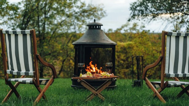 A campfire with a grill and two striped chairs in a grassy area.