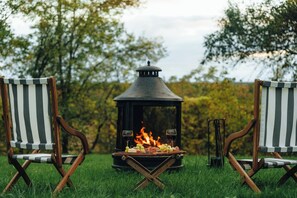 A campfire with a grill and two striped chairs in a grassy area.