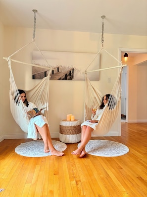 Two people relaxing in a room with a wooden floor, a round woven ottoman, and a hanging chair. - LE HAVRE BORÉAL (Grondines)