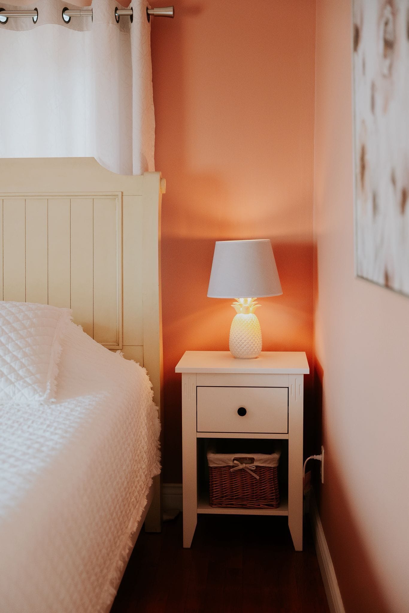A bedroom with a bed, a nightstand with a lamp, a wall-mounted shelf, and a framed picture.
