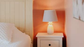 A bedroom with a bed, a nightstand with a lamp, a wall-mounted shelf, and a framed picture.