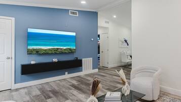 A modern living room with a flat-screen TV, a black entertainment unit, a glass coffee table, and a white armchair.