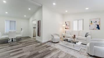 A modern living room with a dining area, white walls, wooden flooring, and contemporary furniture.