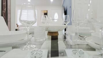 A dining table with clear glassware and white plates, set in a modern interior with a reflective surface.