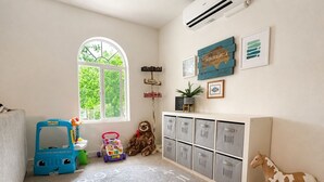 Een kinderkamer met een groot raam, opbergkasten en een vloerkleed met cijfers.