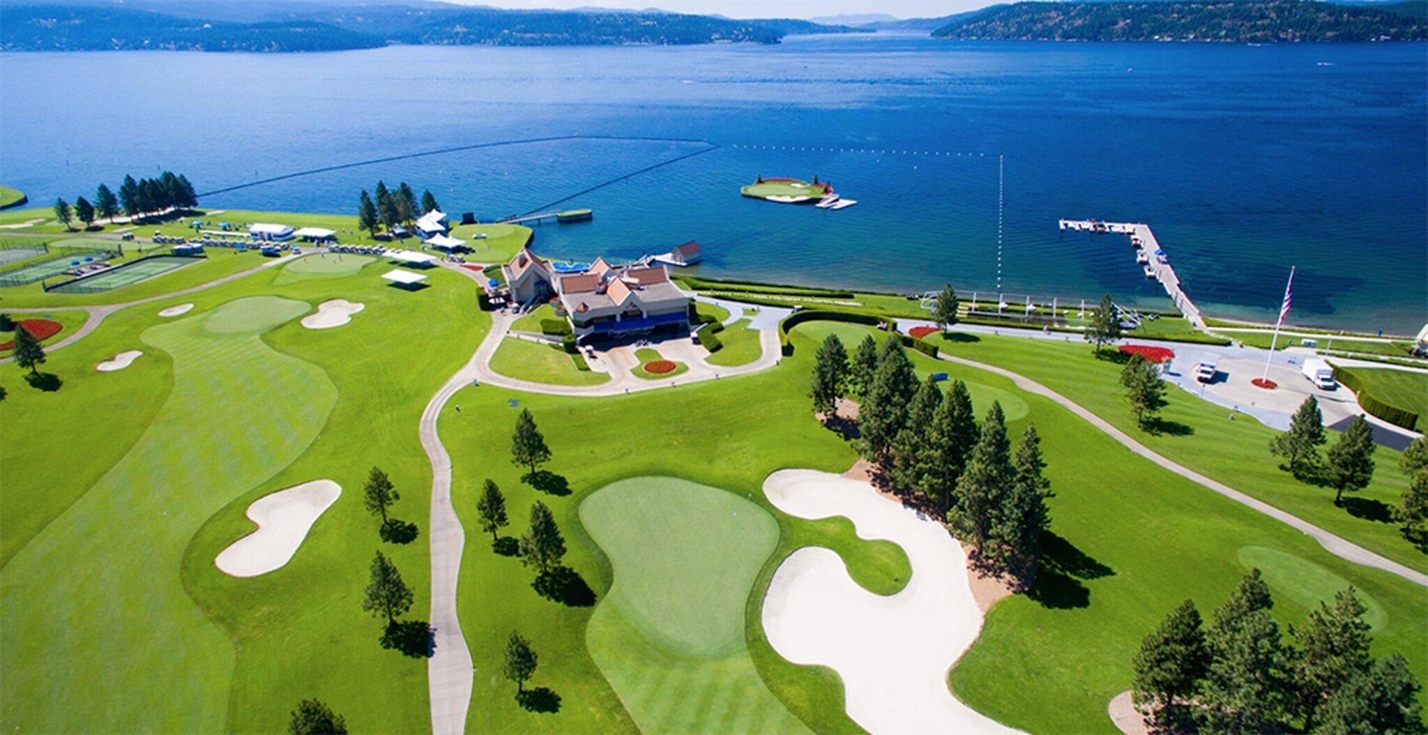 Un parcours de golf avec des bunkers, un club-house et une étendue d’eau en arrière-plan.