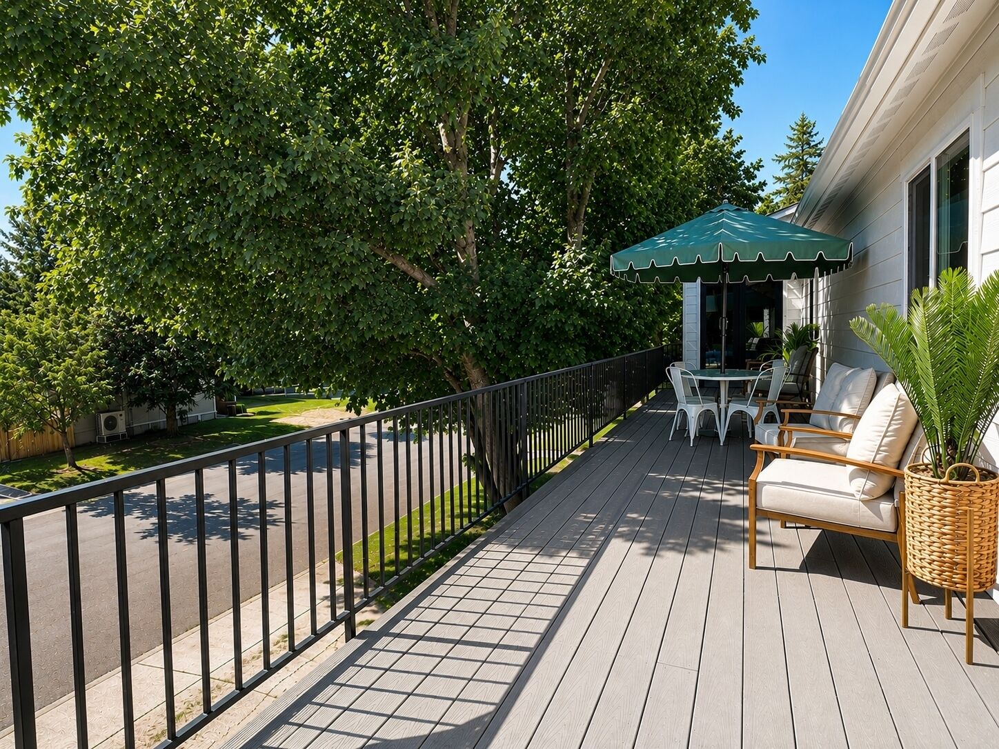 A deck with outdoor furniture, a green umbrella, and a view of a tree-lined street.