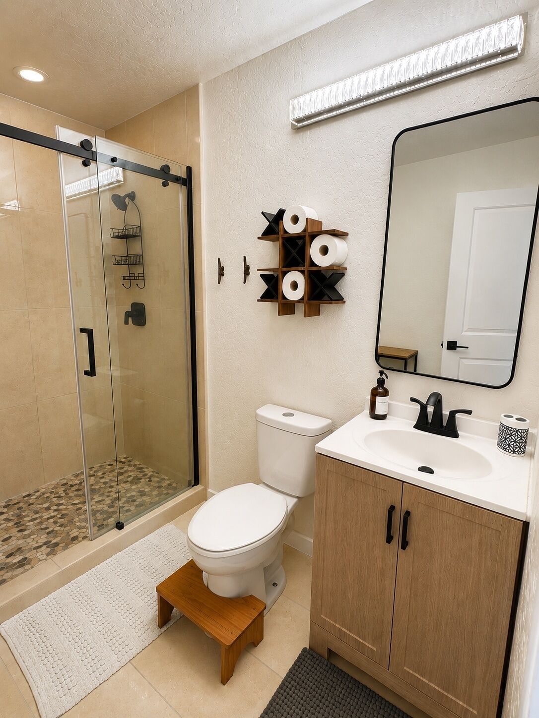 Une salle de bain moderne avec une douche à parois de verre, des toilettes, un lavabo avec un miroir et un meuble-lavabo en bois.
