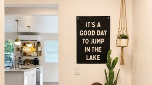 Een gang die leidt naar een keuken, met een bord aan de muur en een kleine houten tafel met een plantje.