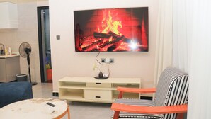 Un salon avec un téléviseur fixé au mur, un canapé, une petite table ronde et un ventilateur.