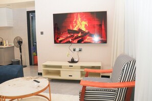 Una sala de estar con un televisor montado en la pared, un sofá, una mesita redonda y un ventilador.