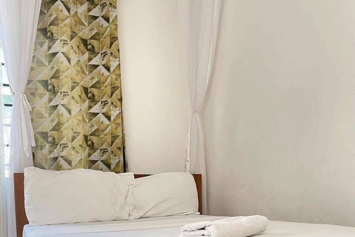 A neatly made bed with white linens and a folded towel, a wooden headboard, and a geometric-patterned wall behind it.