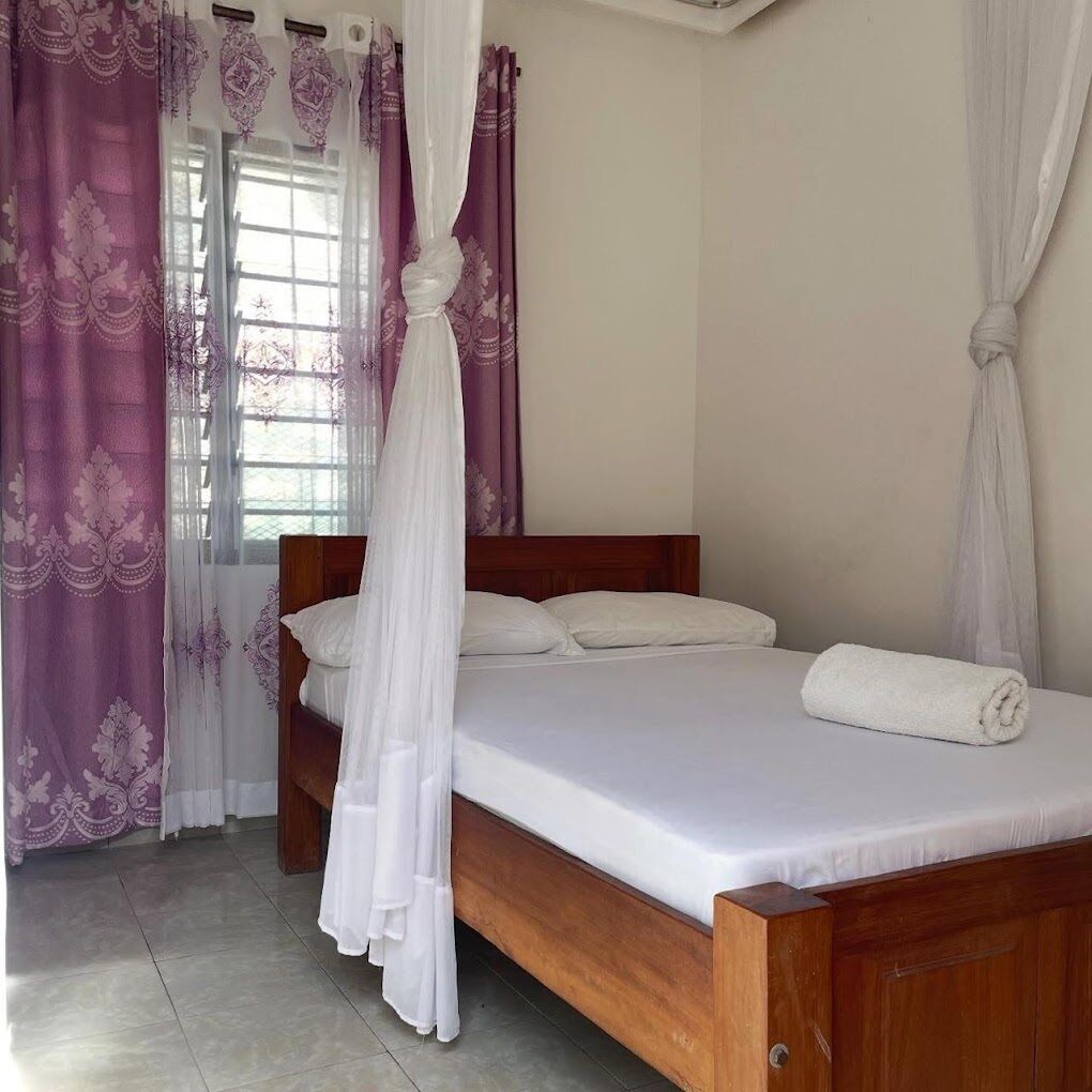 Un dormitorio con cama de madera, ropa de cama blanca y cortinas púrpuras.