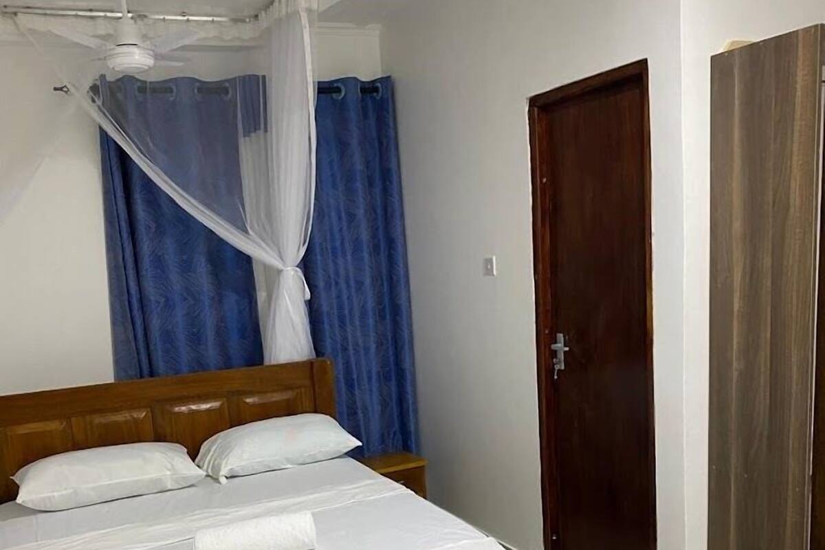 A bedroom with a wooden bed, white bedding, a ceiling fan, and a blue curtain.