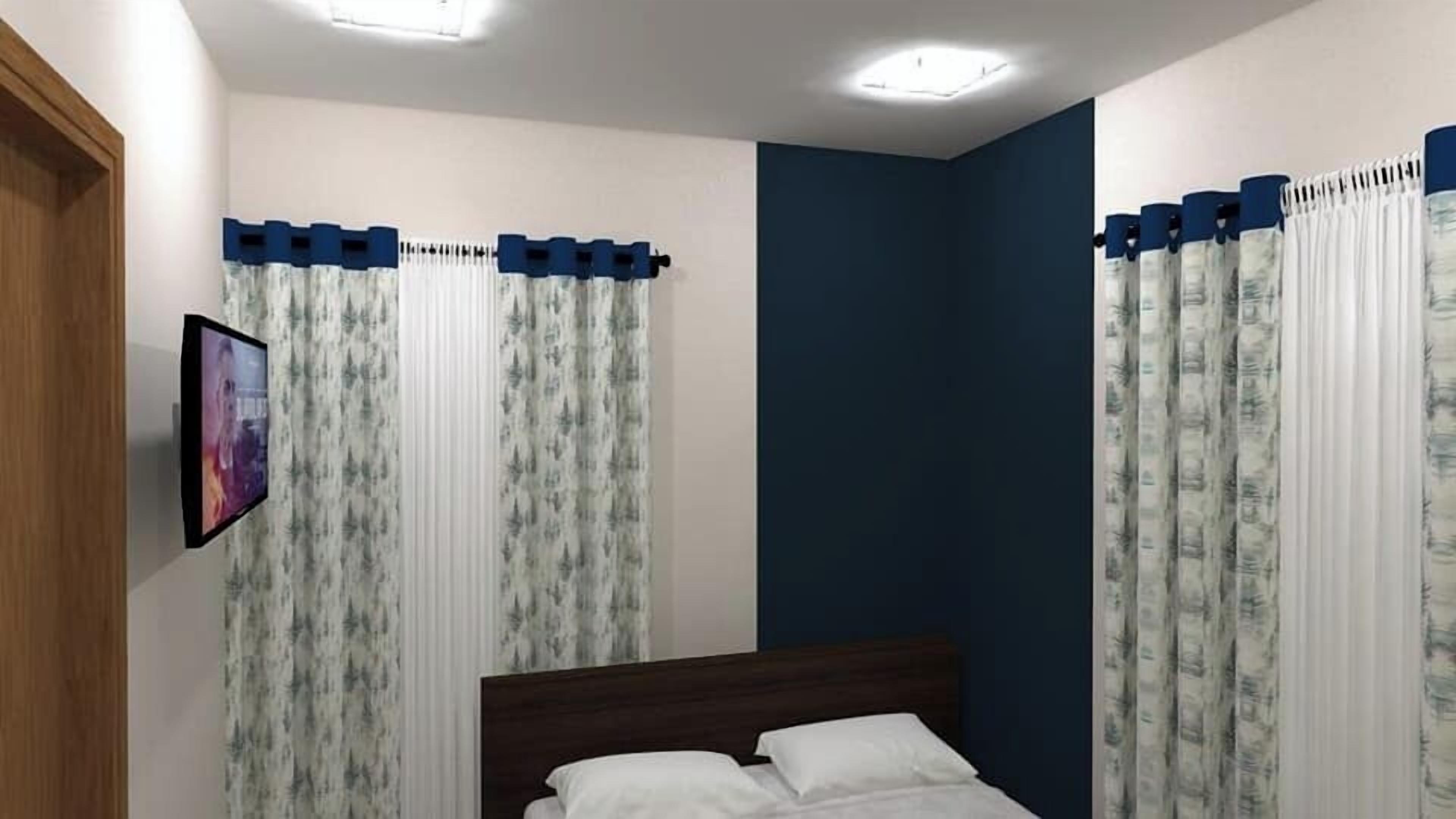 A bedroom with a bed, curtains, a TV, and a blue accent wall.