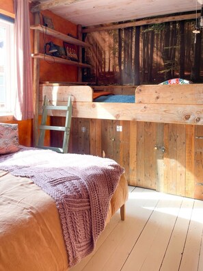 Un dormitorio rústico tipo cabaña con literas, paredes de madera, una escalera y vistas a un bosque.