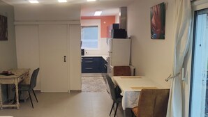 Huone, jossa on ruokapöytä, tuoleja, keittiöalue kaappeineen ja jääkaappi sekä liukuovi.