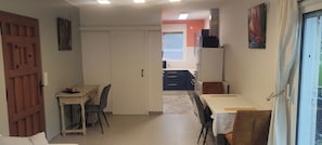 A room with a dining table, chairs, a kitchen area with cabinets, a refrigerator, and a sliding door.