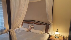 Een bed met hemelbed, een bedlamp en een sierkussen met bloemen.
