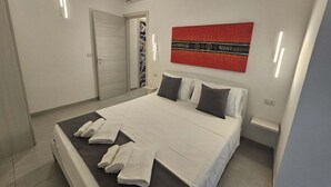 A modern bedroom with a bed, towels, a red artwork, and a white air conditioning unit. - Apartment 5 - Diletta's Residence (Sant'Isidoro)