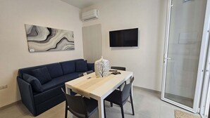 A room with a sofa, a table, chairs, a TV, and a sliding glass door. - Apartment 5 - Diletta's Residence (Sant'Isidoro)
