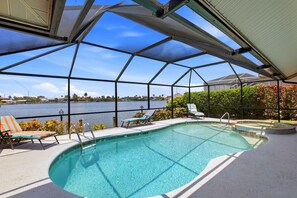 Ein Schwimmbad mit Glasveranda, Blick auf einen See und ein Liegestuhl am Pool.