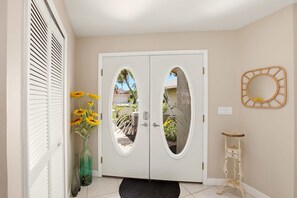 A hallway with a double door, a vase with flowers, a small table, and a wall-mounted mirror. - Cape Escape Home (jacuzzi) (Cape Coral)