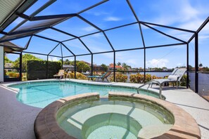 Ein Poolbereich mit Glasveranda, Liegestühlen und Blick auf ein Gewässer.