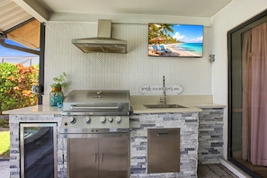 An outdoor kitchen with a built-in grill, a sink, and a herringbone-patterned backsplash. - Cape Escape Home (jacuzzi) (Cape Coral)