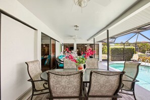 Eine überdachte Terrasse mit Esstisch und Stühlen, im Hintergrund ein Pool und Blick ins Grüne.