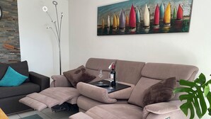 Un soggiorno moderno con un divano reclinabile, un tavolino da caffè, un quadro con dei velieri e una pianta.