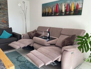 Ein modernes Wohnzimmer mit einer Liegesofa, einem Couchtisch, einem Gemälde von Segelbooten und einer Pflanze.