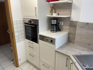 Eine kompakte Küche mit Geschirrspüler von Bosch, einer Kaffeemaschine und einem Einbauofen.