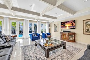 Ein geräumiges Wohnzimmer mit einem Glastisch, blauen Sofas, einem Fernseher und Blick auf einen Pool.