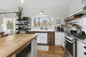 A modern kitchen with a wooden island, stainless steel appliances, and a large window. - Cozy Luxury Farmhouse, Minutes To Downtown & BRPW (Asheville)