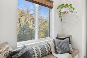 Ein Zimmer mit einem großen Fenster, einer gepolsterten Sitzbank mit gemusterten Kissen und einer hängenden Pflanze.