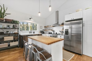 A modern kitchen with a wooden island, stainless steel appliances, and a view of trees outside. - Cozy Luxury Farmhouse, Minutes To Downtown & BRPW (Asheville)