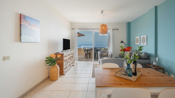 A modern living room with a wooden dining table, a TV, and a view of the sea through a glass door. - Vacation Home 'Vistamar-lovely Renovated With' with Wi-Fi (La Matanza de Acentejo)