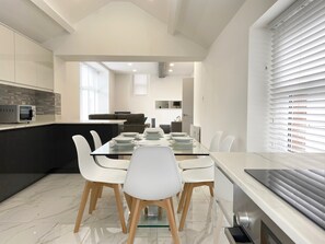 A modern kitchen with a dining area, a built-in microwave, and a large window with blinds. - Coniston House by Guestz (Appleby-in0Westmorland)