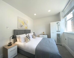 A modern bedroom with a bed, bedside tables, a lamp, a wardrobe, and a window. - Coniston House by Guestz (Appleby-in0Westmorland)