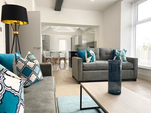 A modern living room with a grey sofa, patterned cushions, a coffee table, and a floor lamp. - Coniston House by Guestz (Appleby-in0Westmorland)