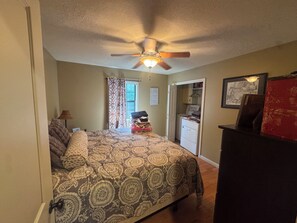Un dormitorio con cama, ventilador de techo, ventana con cortinas, zona de lavandería y cómoda.