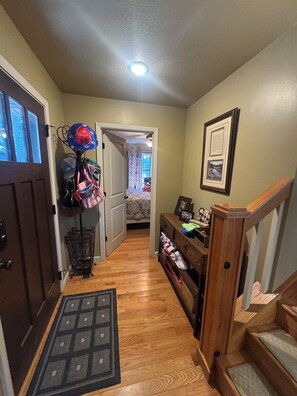 A hallway with a wooden floor, a door on the left, a coat rack with hats, a framed picture on the wall, and a staircase on the right. - "The Hangout" - Perfect for enjoying Tannenbaum Resort & Greers Ferry Lake! (Drasco)