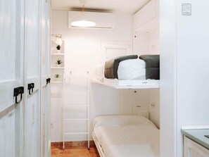 A compact room with a bunk bed, a small shelf with plants, a white door, and a ceiling light. - Airén Harbor's Light (La Vila Joiosa)