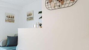 Ein modernes Zimmer mit einer niedrigen weißen Wand, einem Holz-Kopfteil, einem grauen Sofa mit Kissen und zwei gerahmten Kunstwerken.