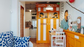 A room with a patterned sofa, a dining table with chairs, a kitchen area, and a mural on the wall. - Cencibel Harbor's Light (La Vila Joiosa)
