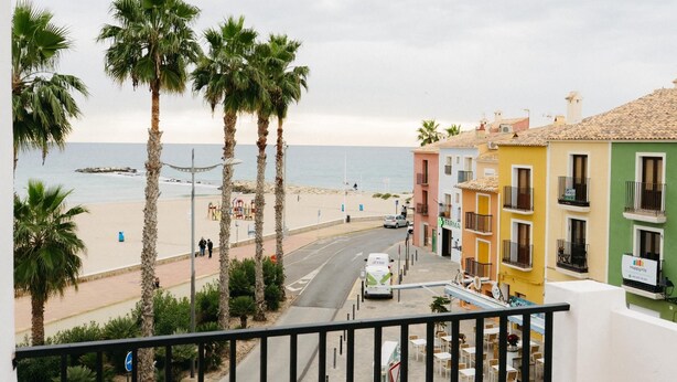 A coastal street with palm trees, colorful buildings, and a view of the beach. - Cencibel Harbor's Light (La Vila Joiosa)