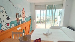 A hotel room with a bed, a dining table with fruits and snacks, a mural, and a view of the beach. - Cencibel Harbor's Light (La Vila Joiosa)